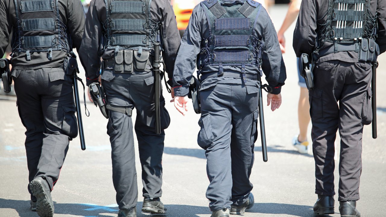 The backs of four police officers wearing tactical gear while walking down a road doing their patrols.