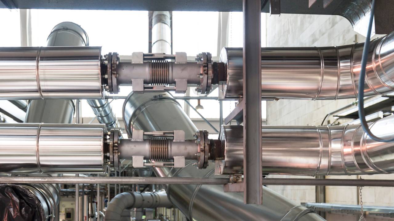 An image of expansion joints connecting an industrial heating system inside of a large building space.