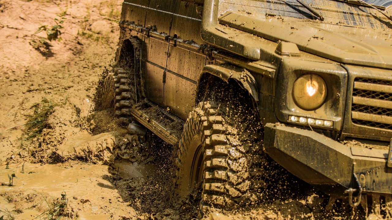 An off-road vehicle with large tires kicking up mud and dirt as it drives on a rocky mountain trail.