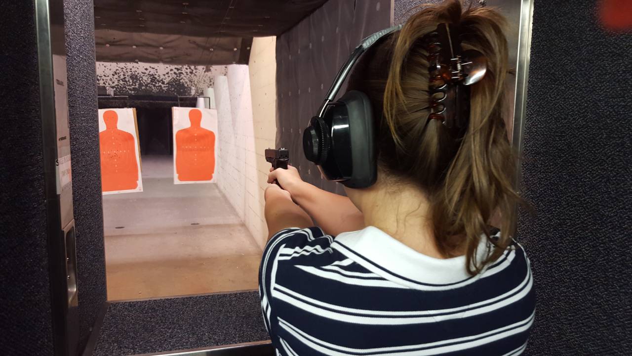 A woman wearing a black and white striped shirt holding a firearm out in front of her while aiming at a target.