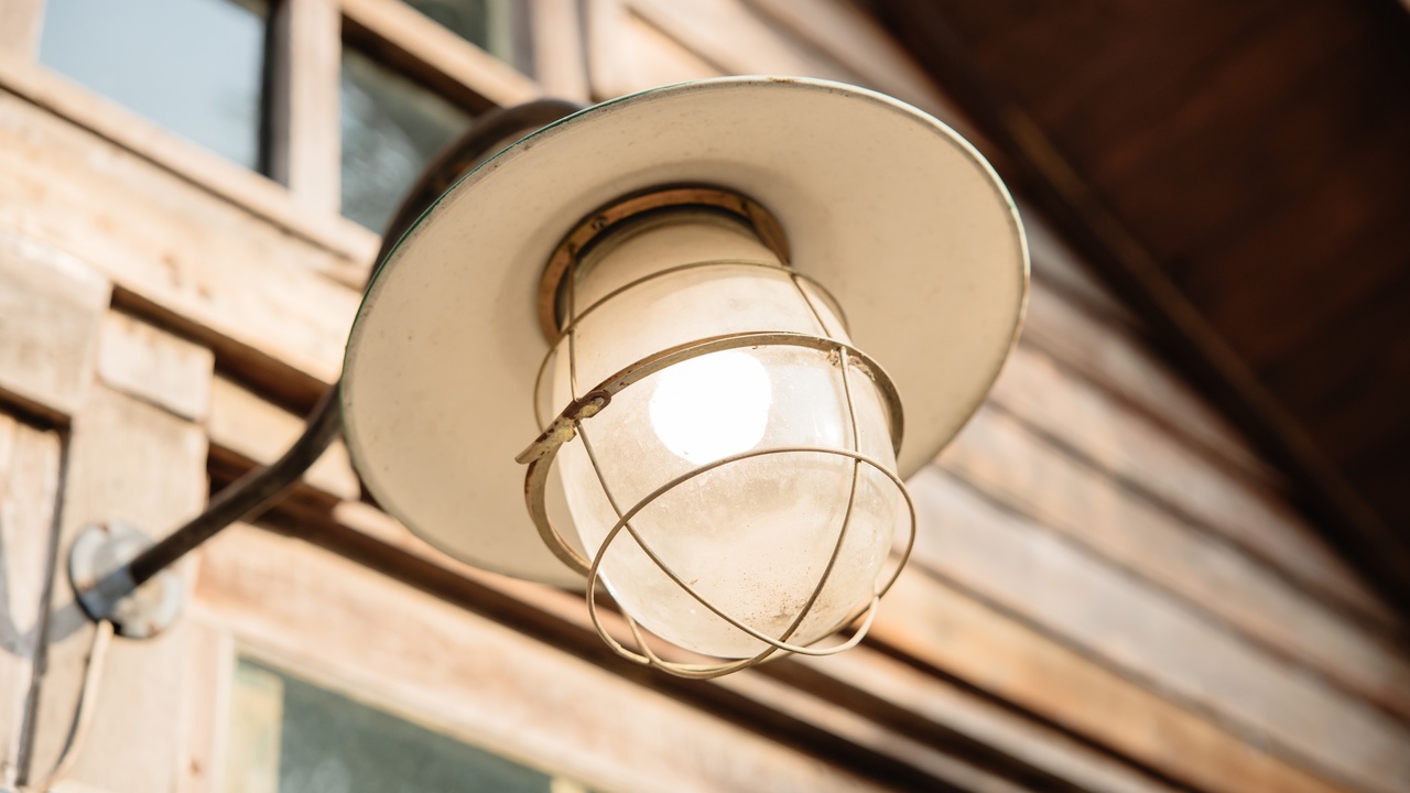 A close-up view shows a light on the outside of a wooden shed. The light has a circular top covering the bulb.