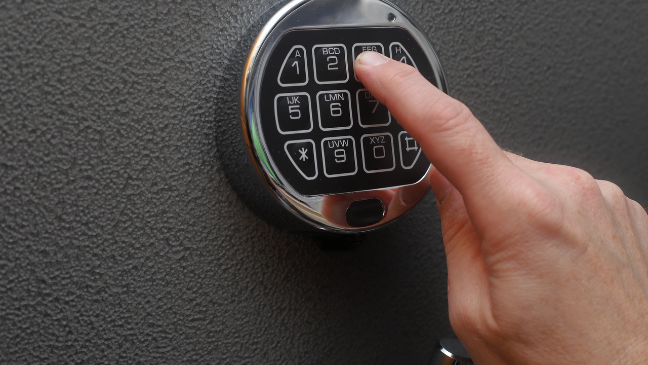 A close-up of a man's hand pressing numbers on a keypad that is attached to a solid, grey, pockmarked surface.