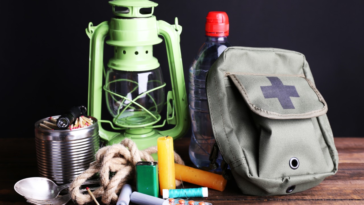 A collection of emergency preparedness supplies sits on the table. There is a lantern, medicine, first aid bag, and candles.
